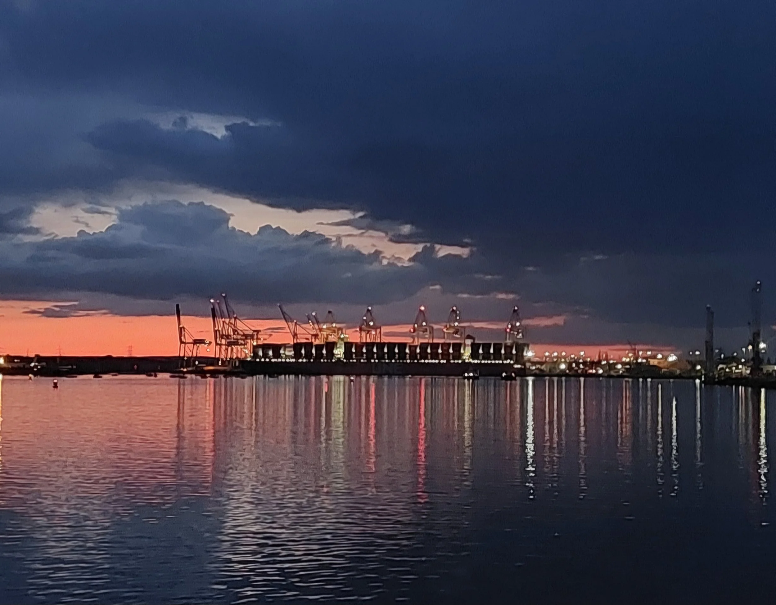 Silhouetted cranes and industrial structures form the background with shimmering lights over the water.