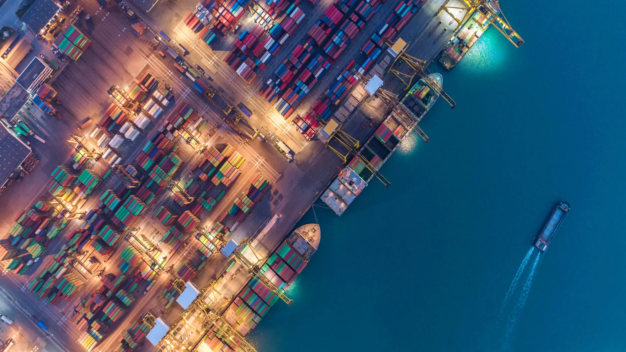 Bird's eye view of a cargo port with stacks of cargo containers and ships in the water off the dock
