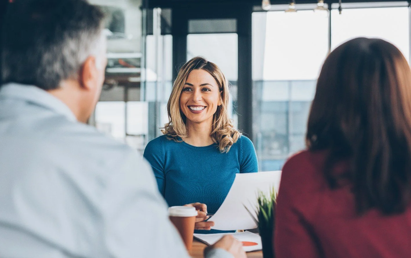 A smiling young professional woman looking toward a man and a woman sitting across from her
