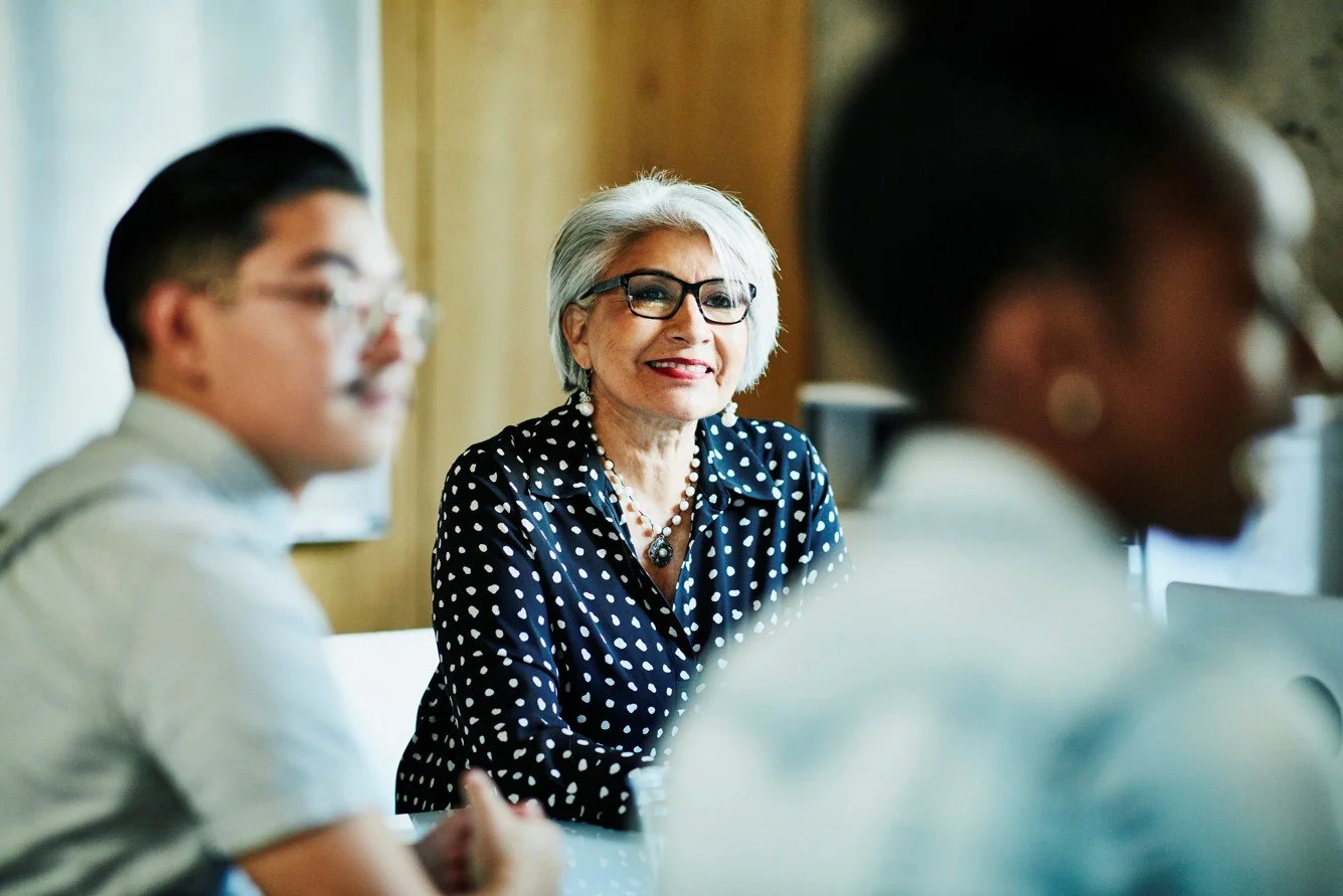 A professional, middle-aged woman looking across at her colleagues, in a professional setting