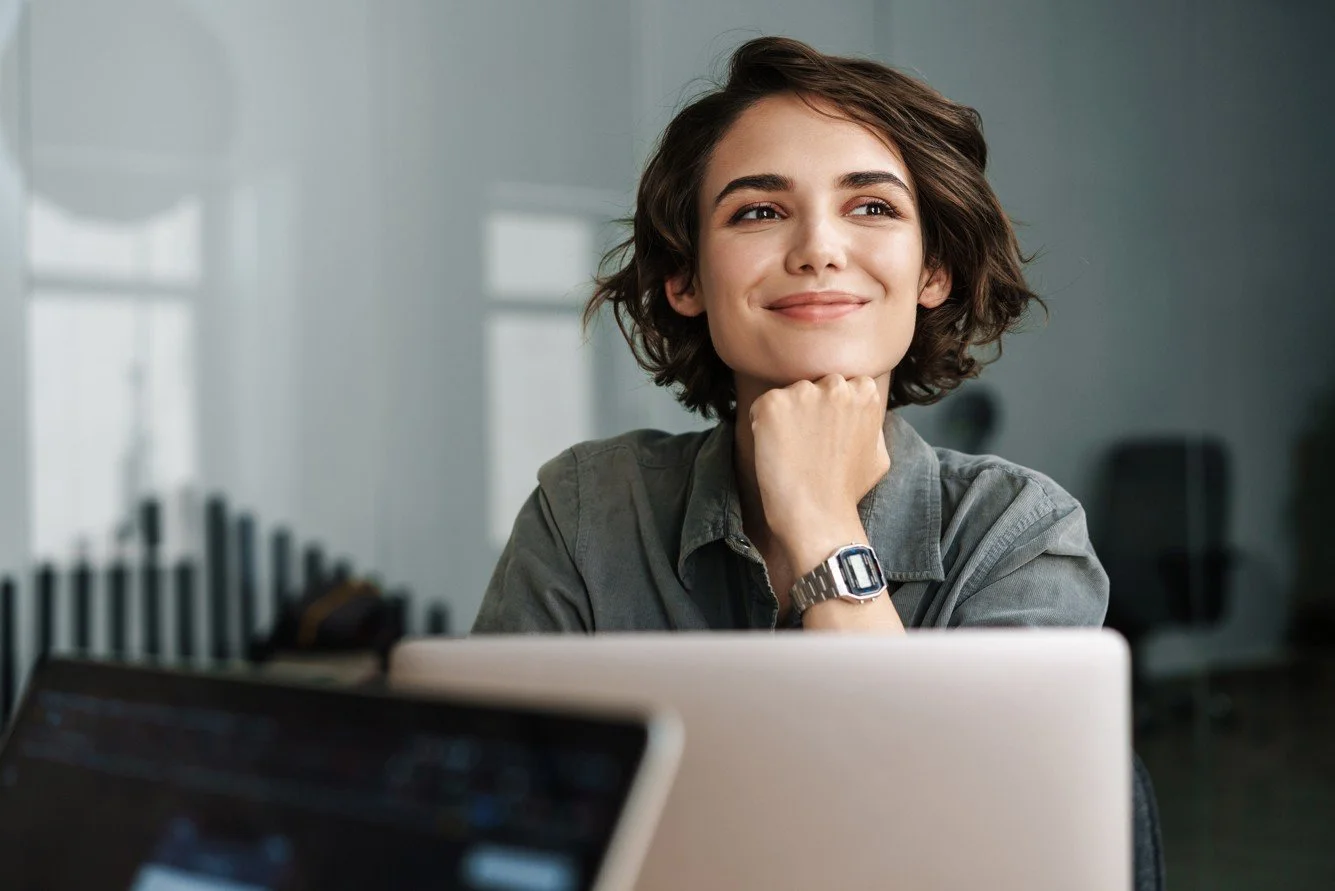 A smiling, young, professional woman resting her chin on her hand