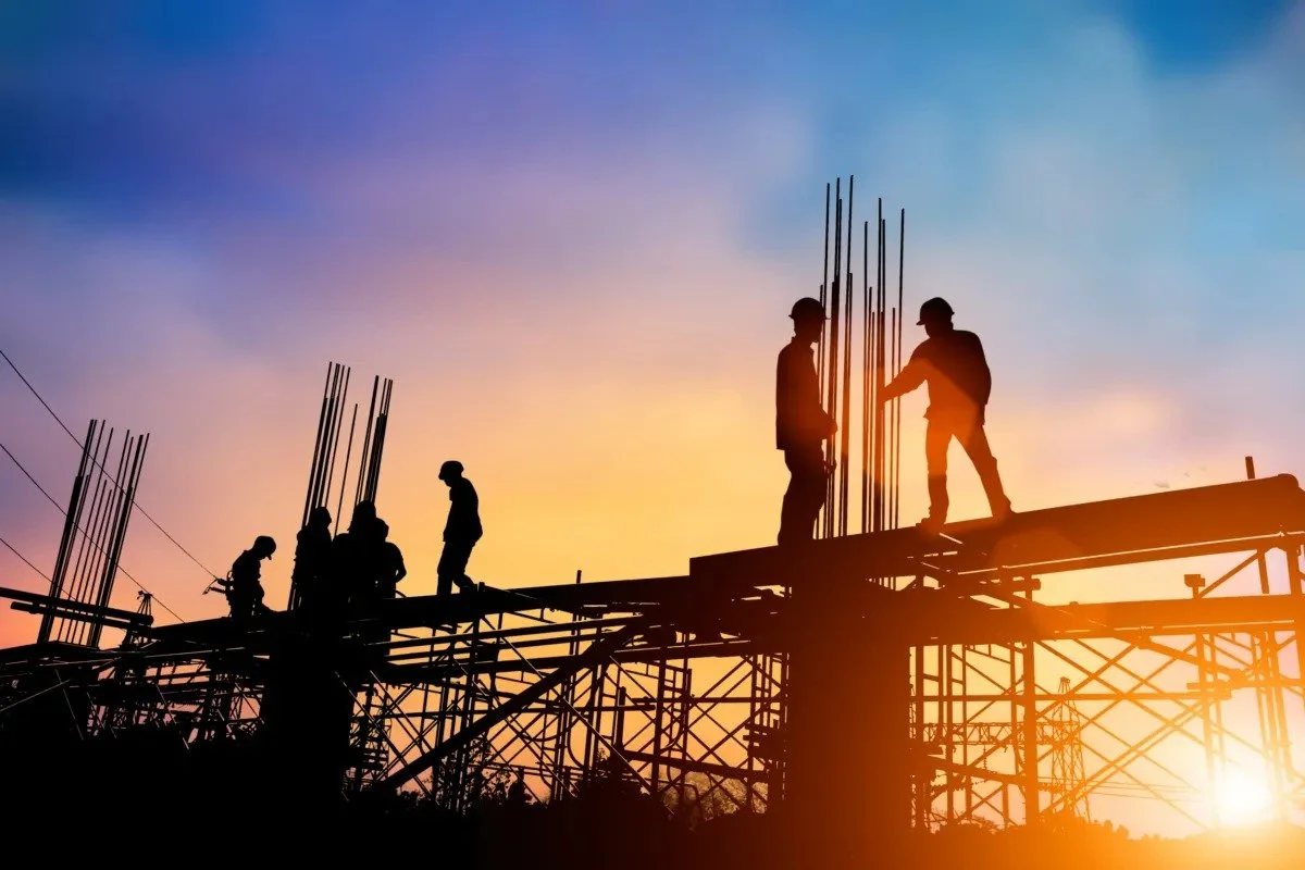 Builders on a construction site with scaffolding, backlit by the rising sun