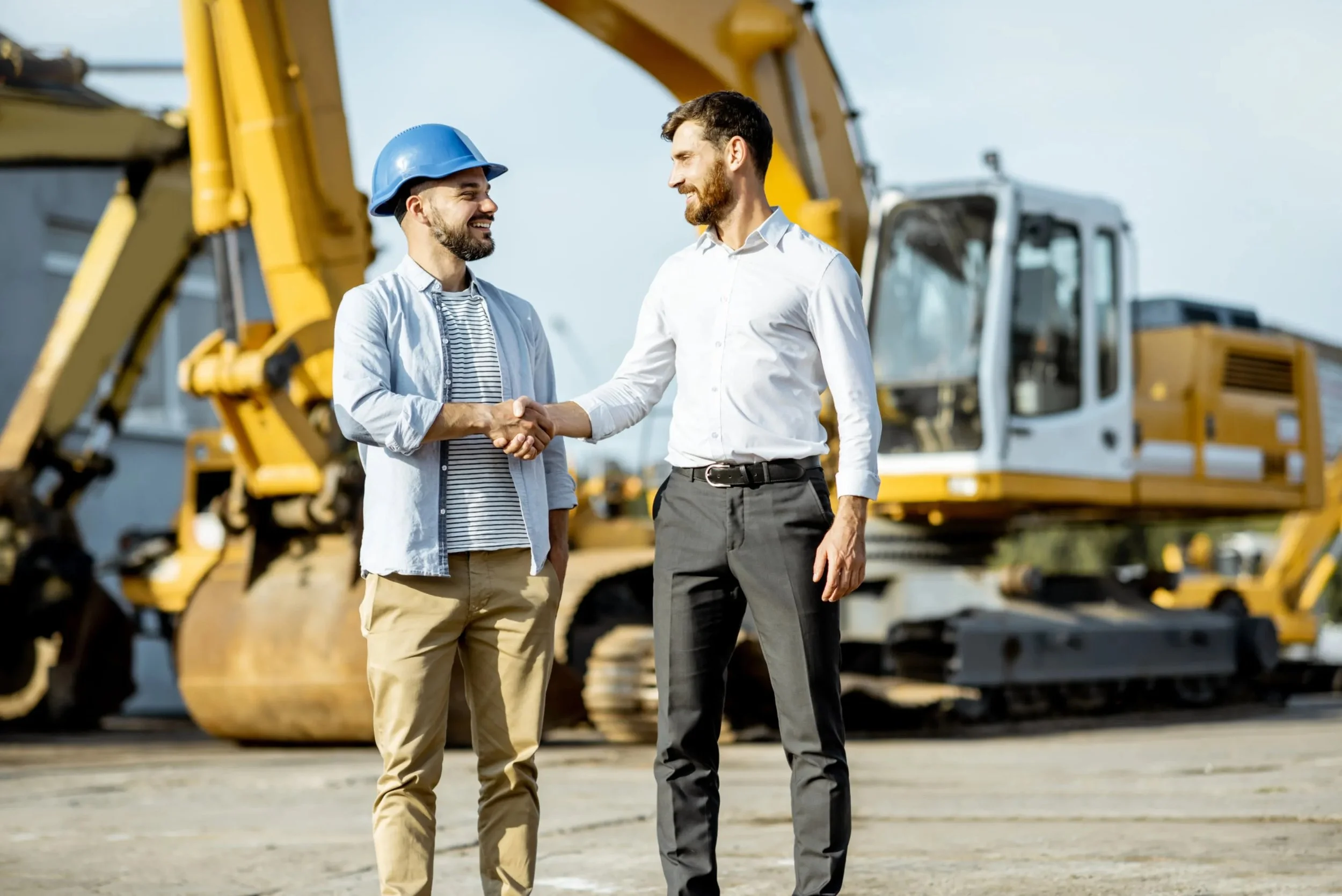 Two professional men shaking hands on a building site, with construction equipment in the background