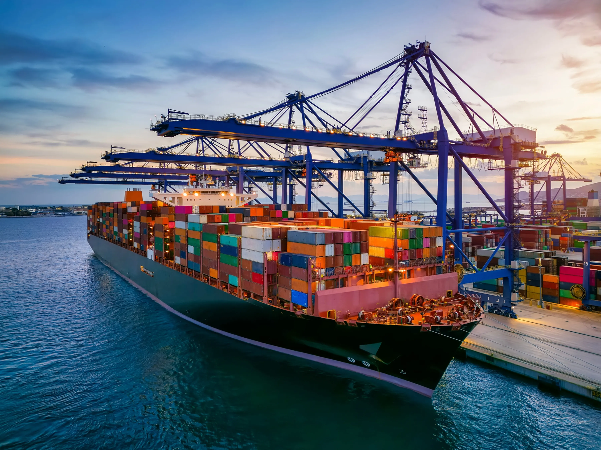 A large container ship docked at a port with cargo cranes positioned overhead