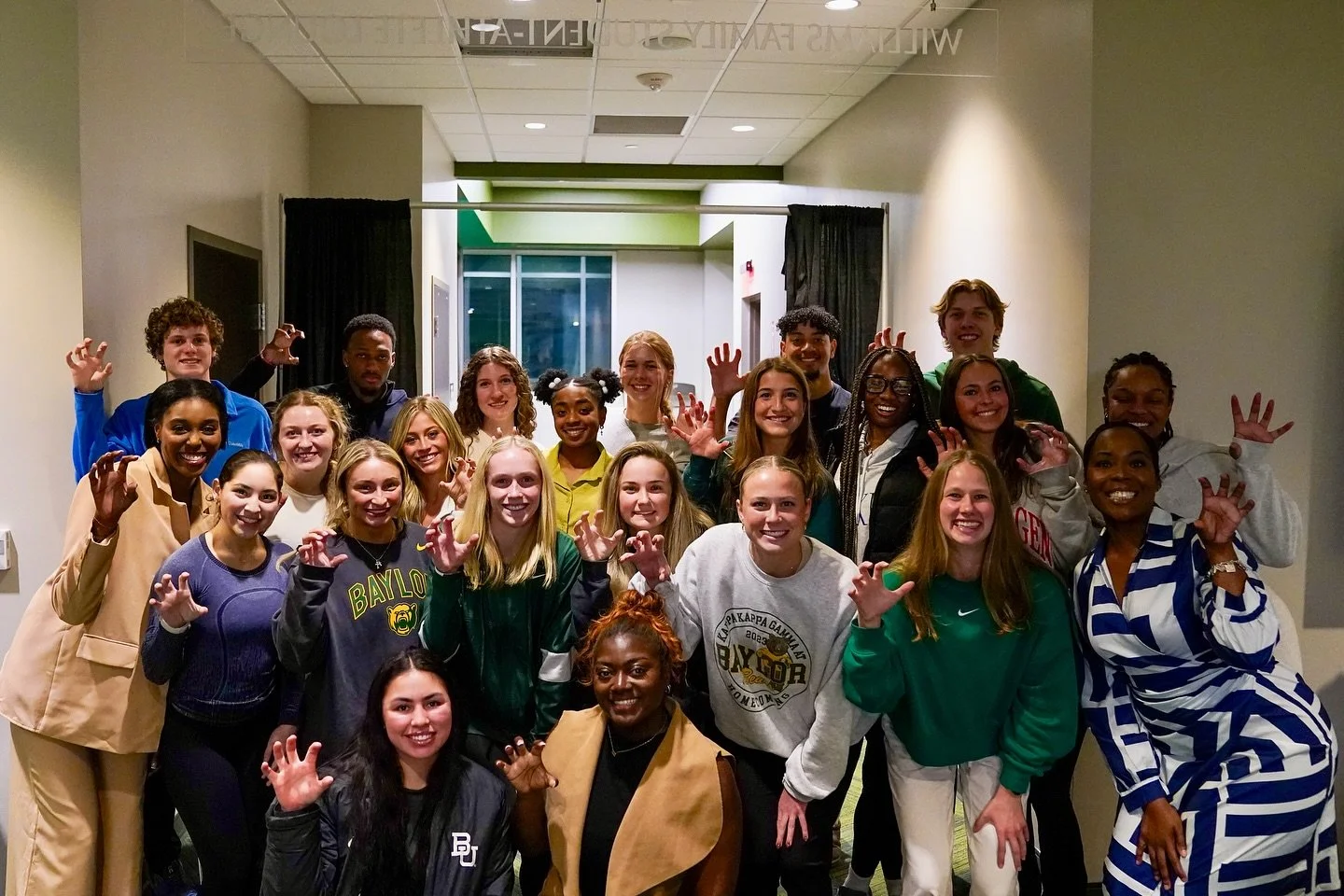 Group of young people posing together indoors, smiling, some making claw-like hand gestures.
