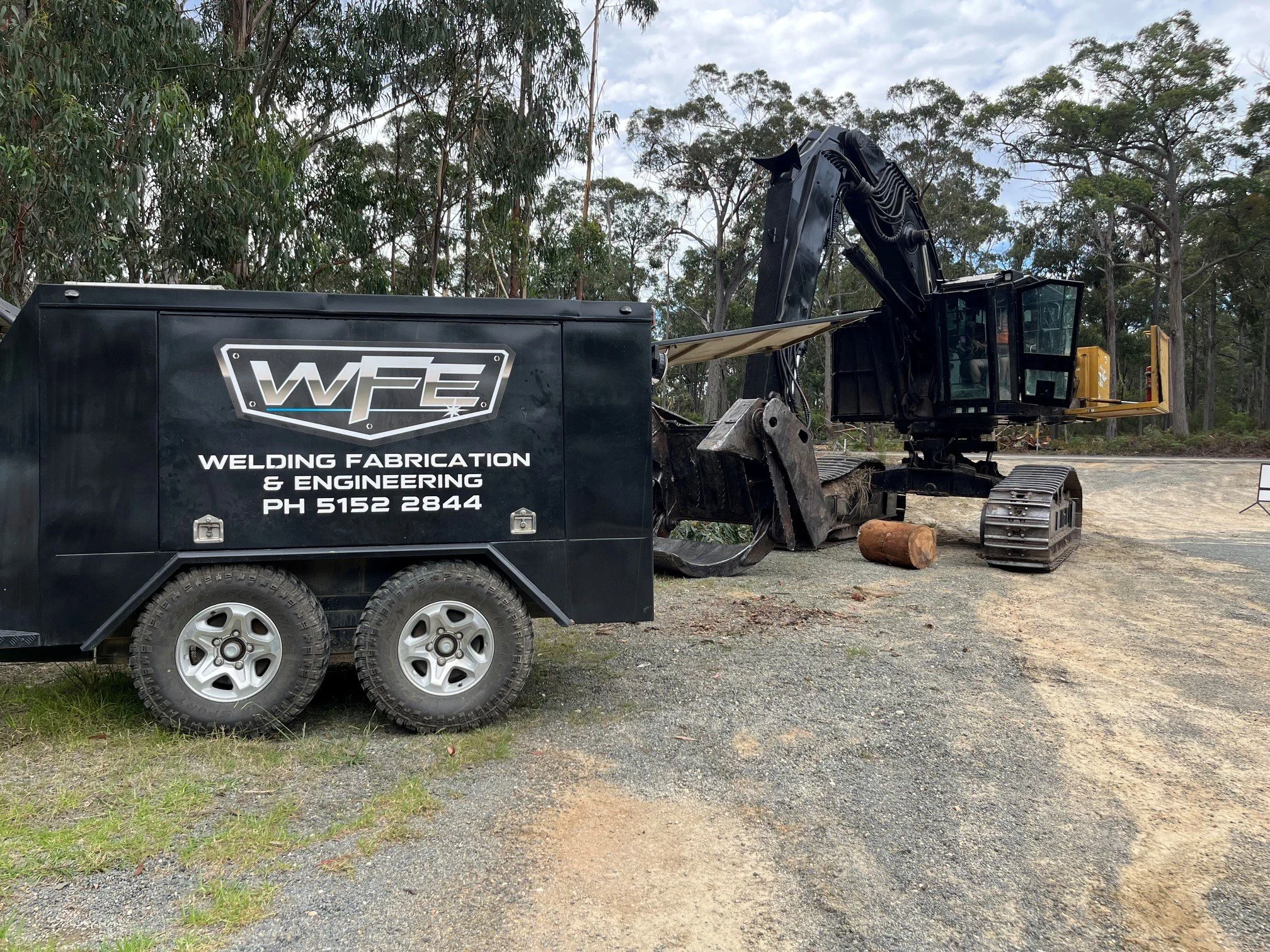 A large black piece of equipment with the logo 'WP2' and the text 'Welding Fabrication & Engineering' on the side. The equipment appears to be a tracked excavator, with a black cab, black arm, and tracks, situated outdoors on a dirt or gravel area with trees and a cloudy sky in the background.