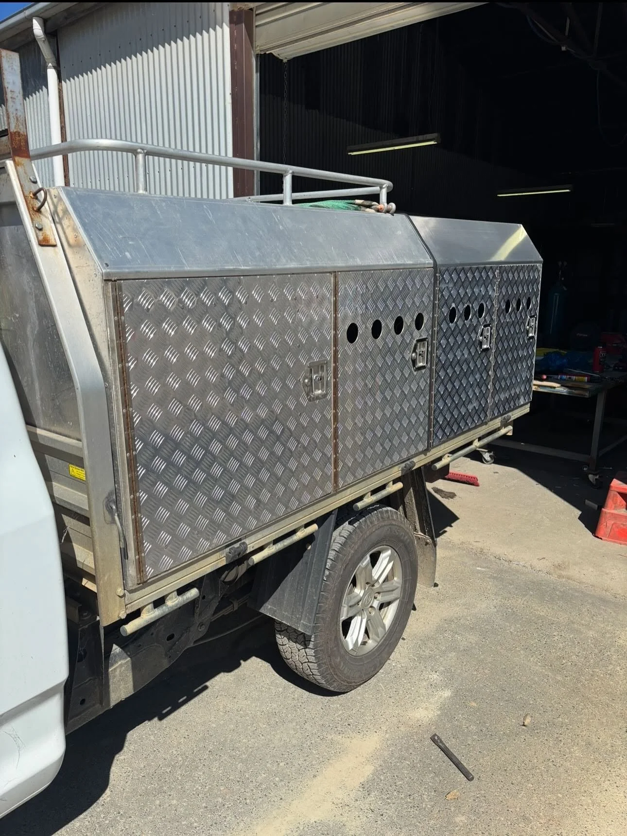 A pickup truck with silver diamond plate storage compartments mounted in the truck bed, parked outside a building with a partially open garage door.