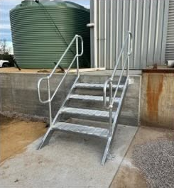 Metal wheelchair-accessible ramp with handrails leading up to a higher level outside a building.