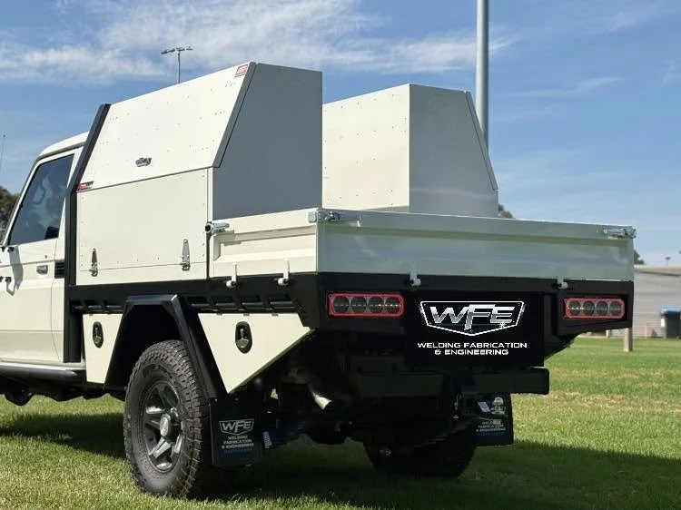 A pickup truck with a custom metal flatbed and storage compartments, parked on grass under a blue sky.