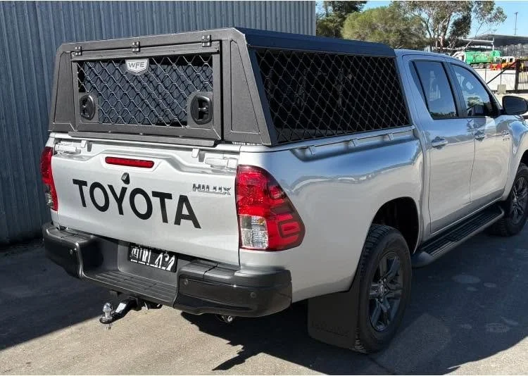 Silver Toyota pickup truck with a black cargo canopy and a large Toyota logo on the tailgate, parked outdoors.
