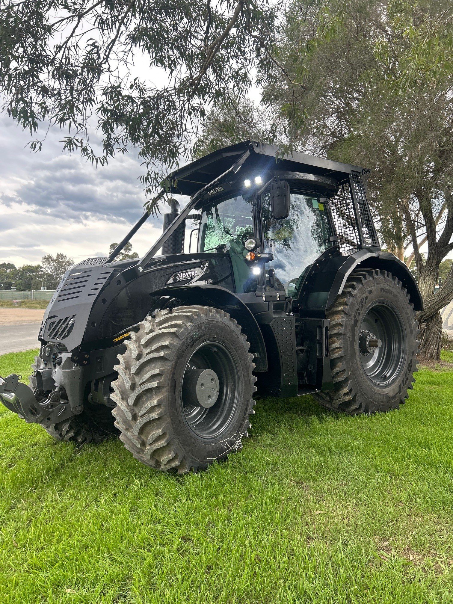 A black tractor parked on a grassy area with trees and cloudy sky in the background.