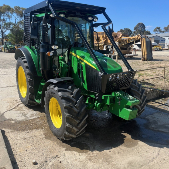 Green and yellow tractor parked outdoors on a concrete surface with construction equipment in the background.