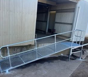 Metal wheelchair ramp outside a metal building with stairs at the top.