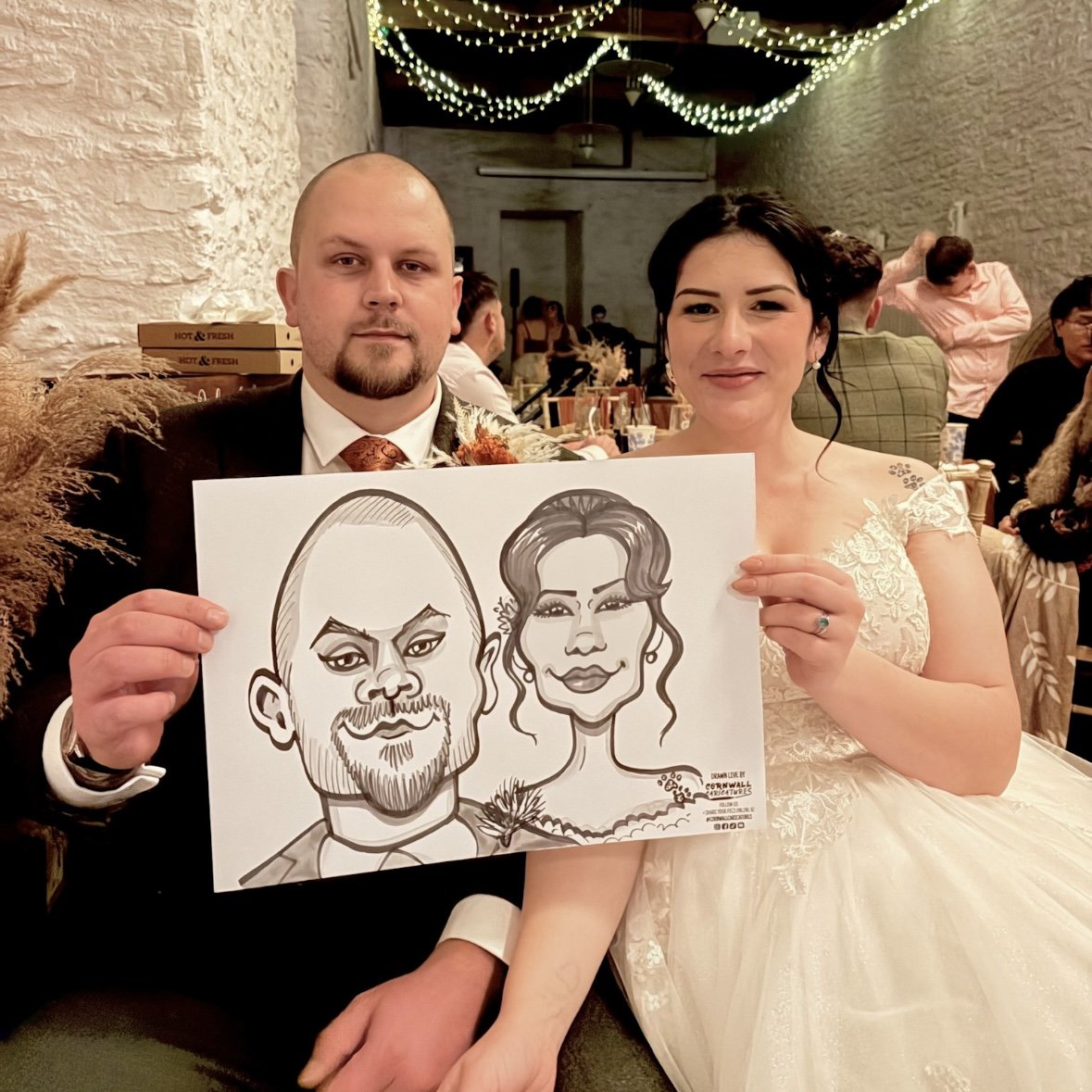 Bride and groom at a wedding reception holding a caricature drawing of themselves.