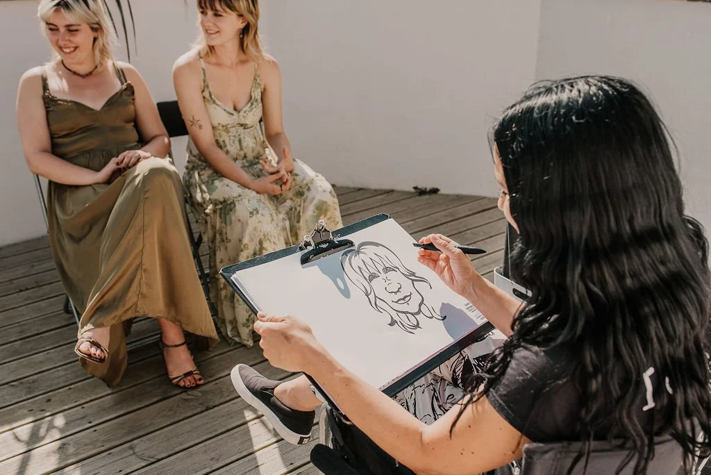 An artist sketching two women sitting on chairs on a wooden deck.