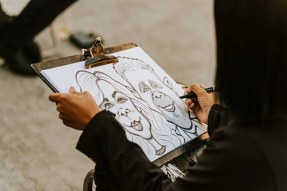 Person sketching a cartoon-style caricature of a smiling woman with long hair and a smiling man with short hair on a clipboard.