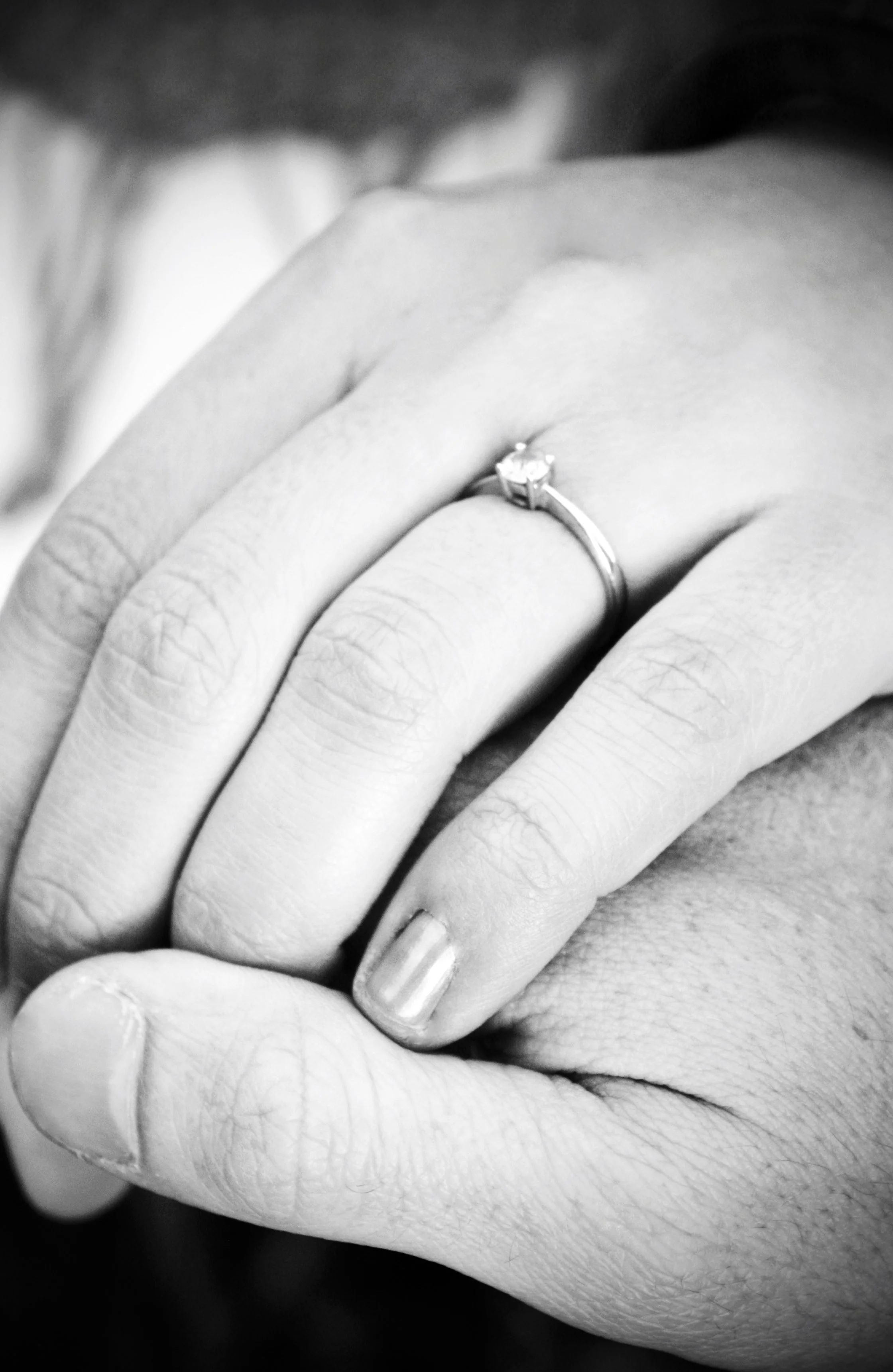 Close-up of a person's hand showing two fingers with a ring on the middle finger, on a textured surface, black and white photograph.