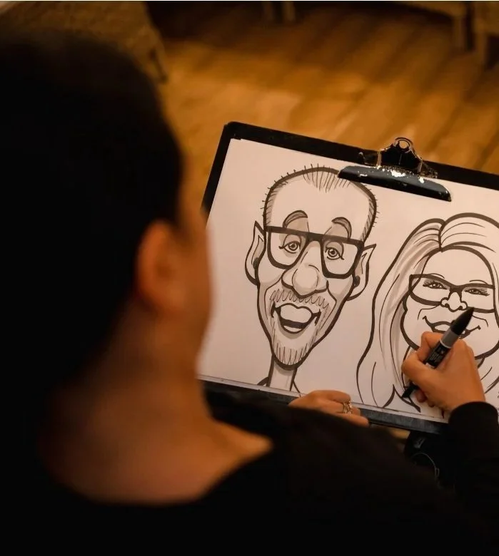 A person drawing caricatures of a man and a woman on a sketchpad.