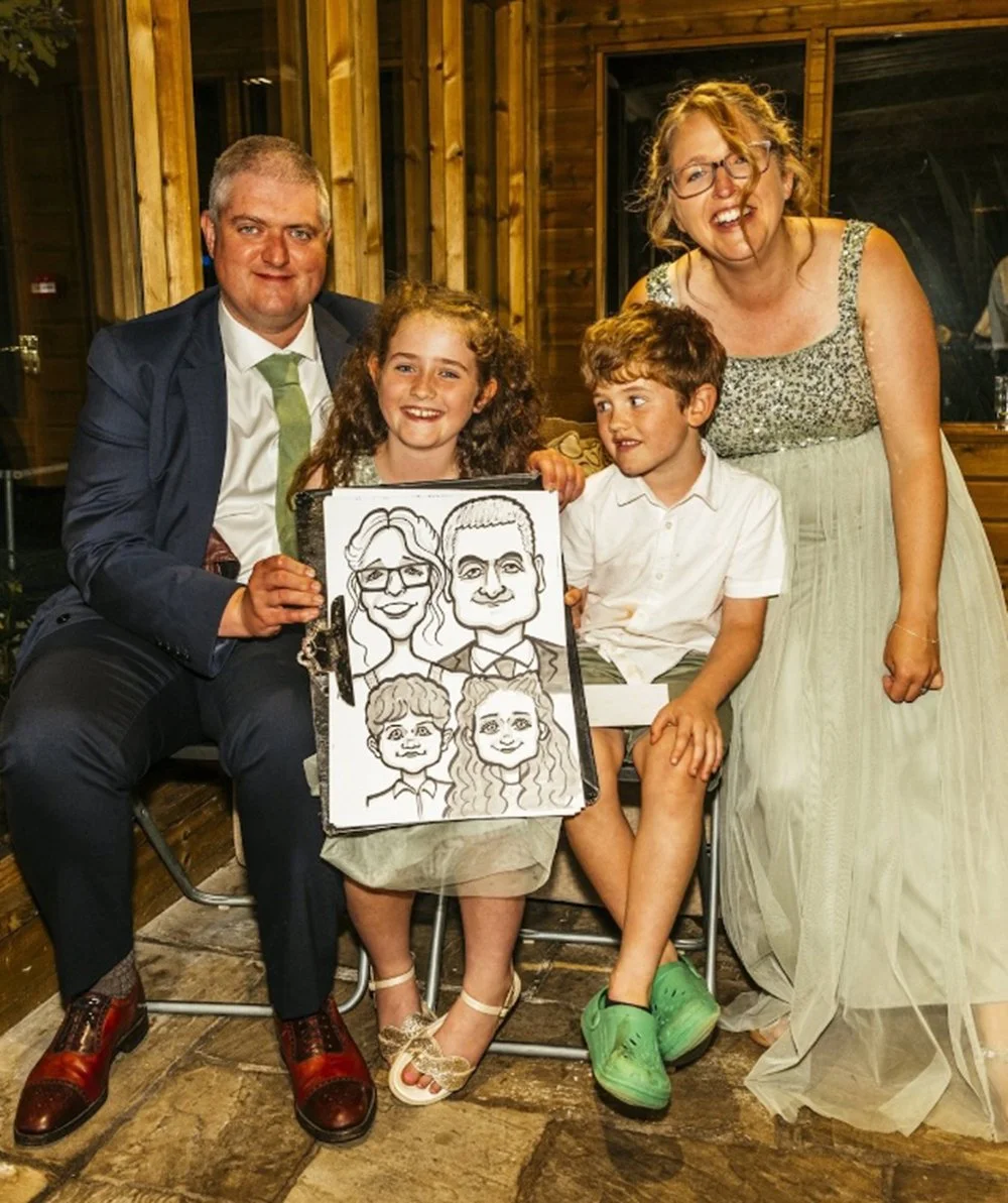 A family of four at a celebration, with the kids holding a large drawing of caricatures of family members.