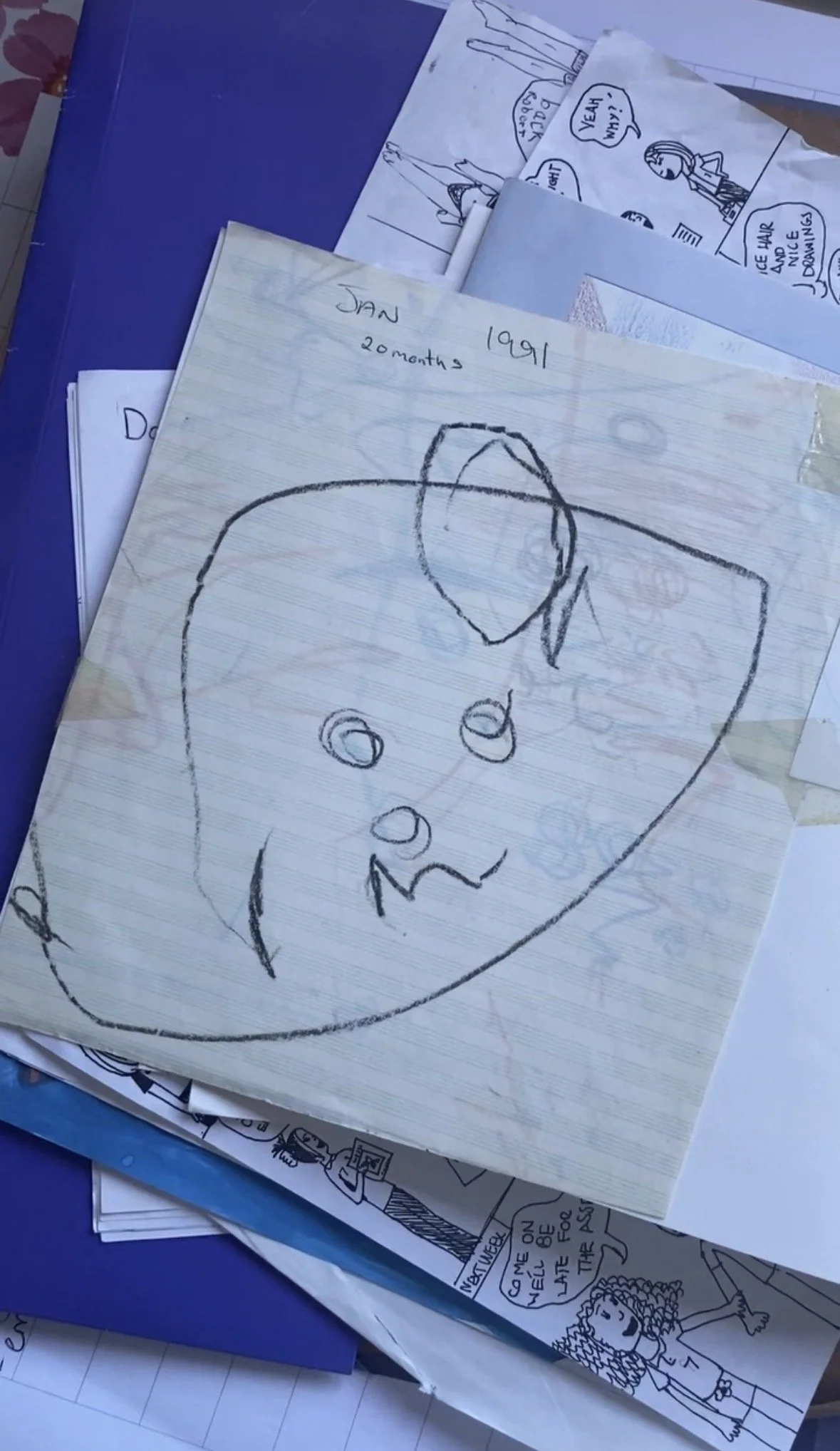 Collection of children's drawings and comic strips on paper, with some drawings of faces, characters, and speech bubbles, placed on top of a blue surface.