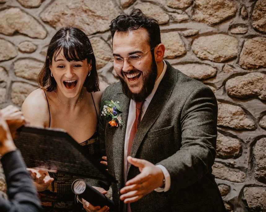 Two people, a woman and a man, are smiling and looking excited while seeing their caricature at an indoor event with a stone wall background.
