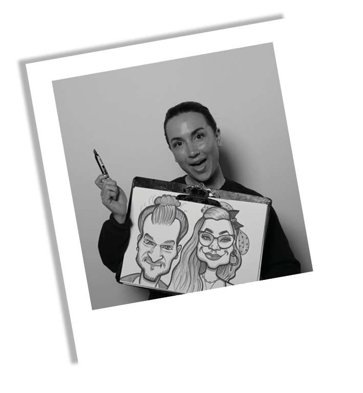 A woman holding a picture of two caricature portraits, one of a man and one of a woman, while smiling and pointing with a pen.