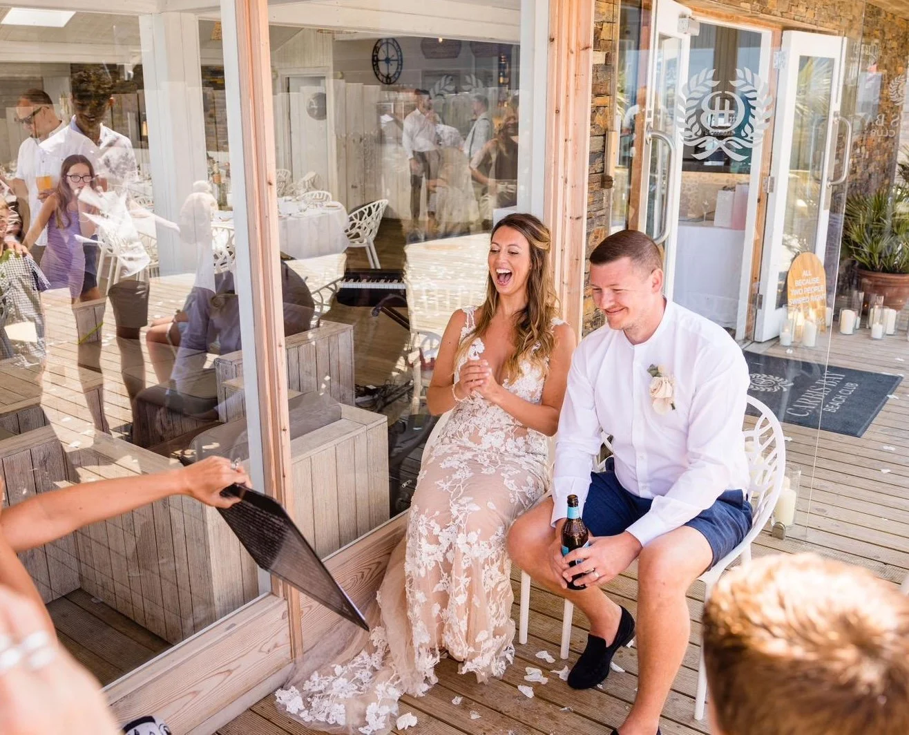 Bride and groom sitting outside during a wedding celebration, smiling and laughing as they are handed a caricature of themselves.