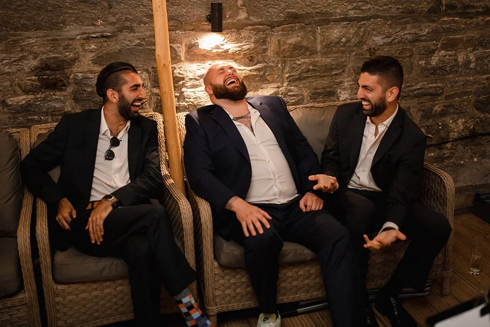 Three men sitting on a wicker sofa laughing and enjoying each other's company in a cozy, rustic setting.