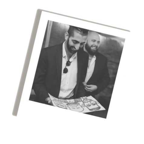 Two men in suits looking at a caricature drawn live at a wedding.