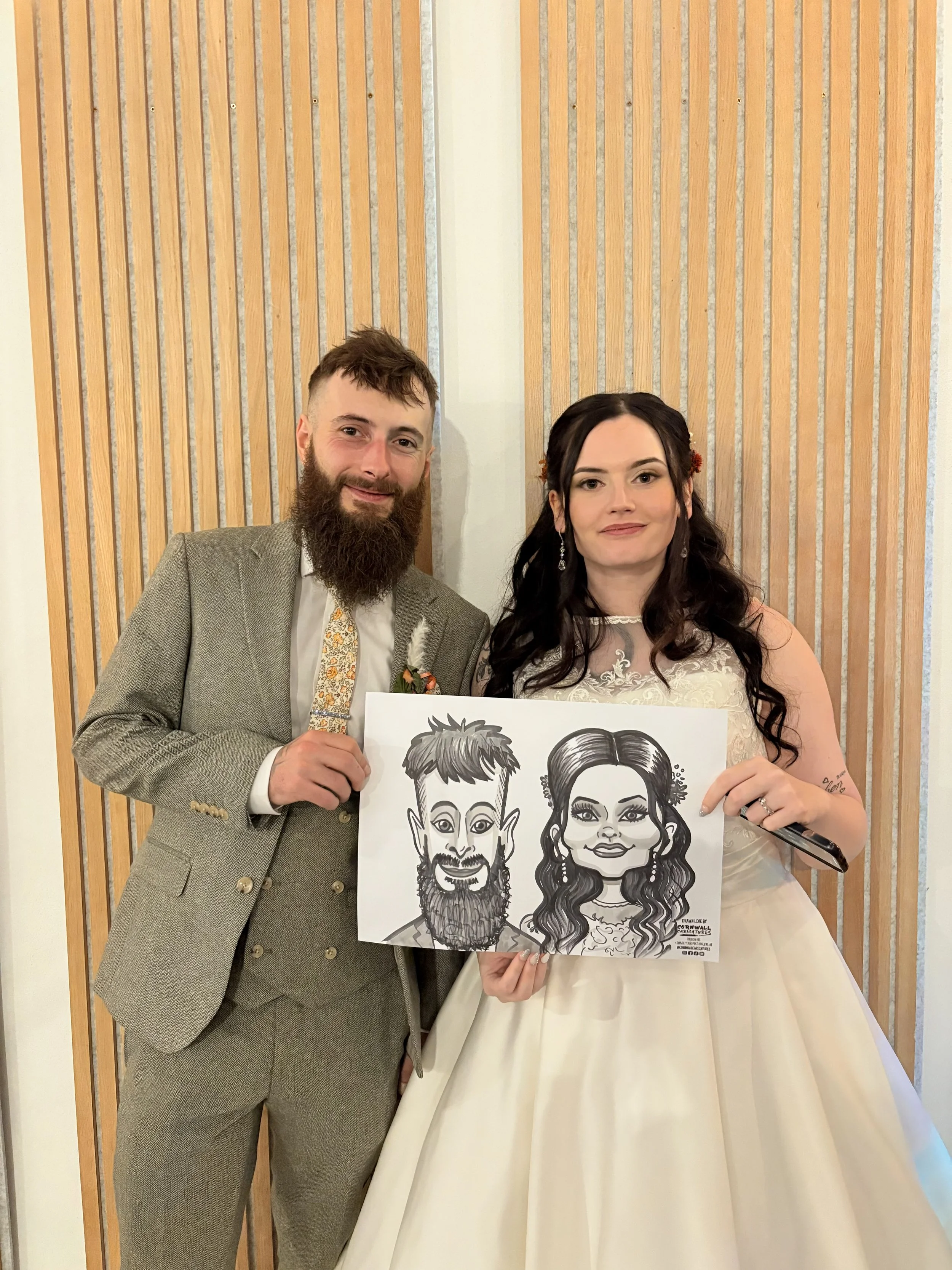 A man and woman in wedding attire holding a caricature drawing of themselves at a celebration or wedding reception.