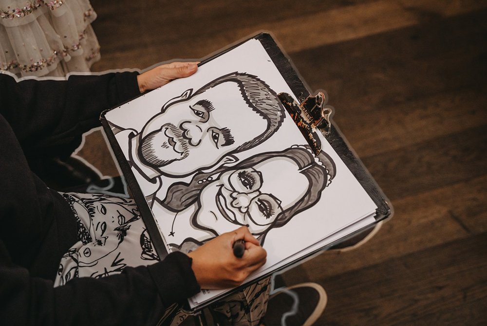Person drawing caricatures of a man and a woman on a flip chart with markers.
