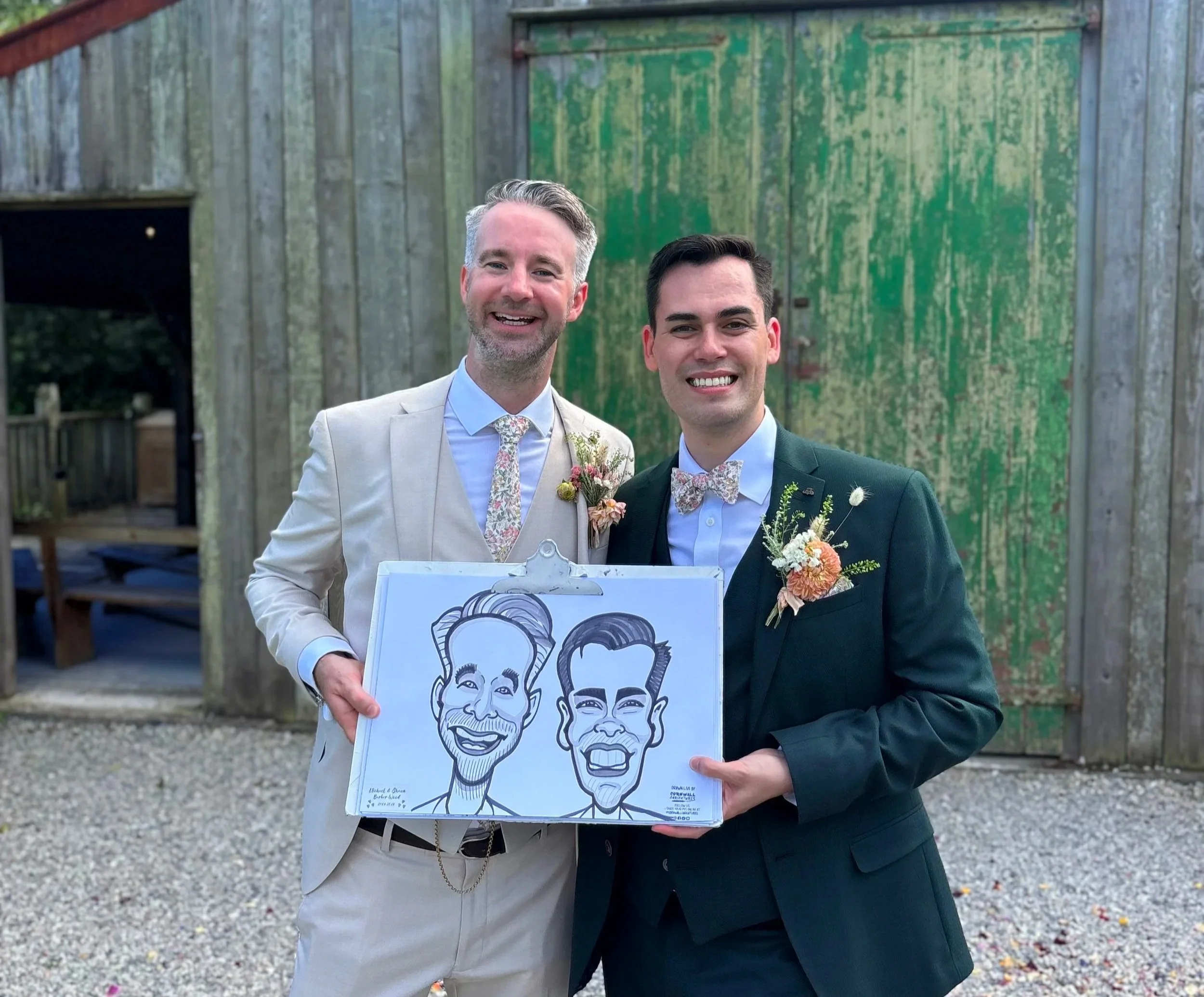Two men in formal attire holding a caricature drawing of themselves at an outdoor event.