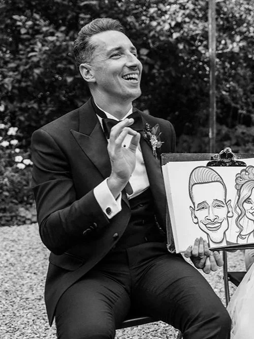 Man in tuxedo at outdoor event holding a framed caricature drawing of himself.