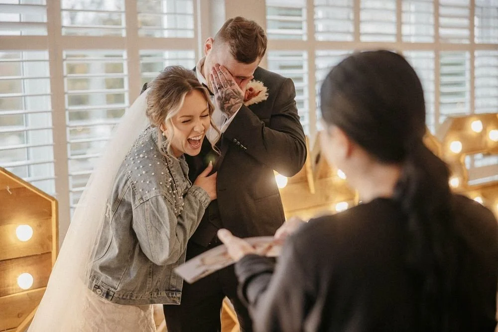 Bride and groom sharing a joyful moment as they see their caricature portrait being revealed at their wedding, in a decorated indoor setting.