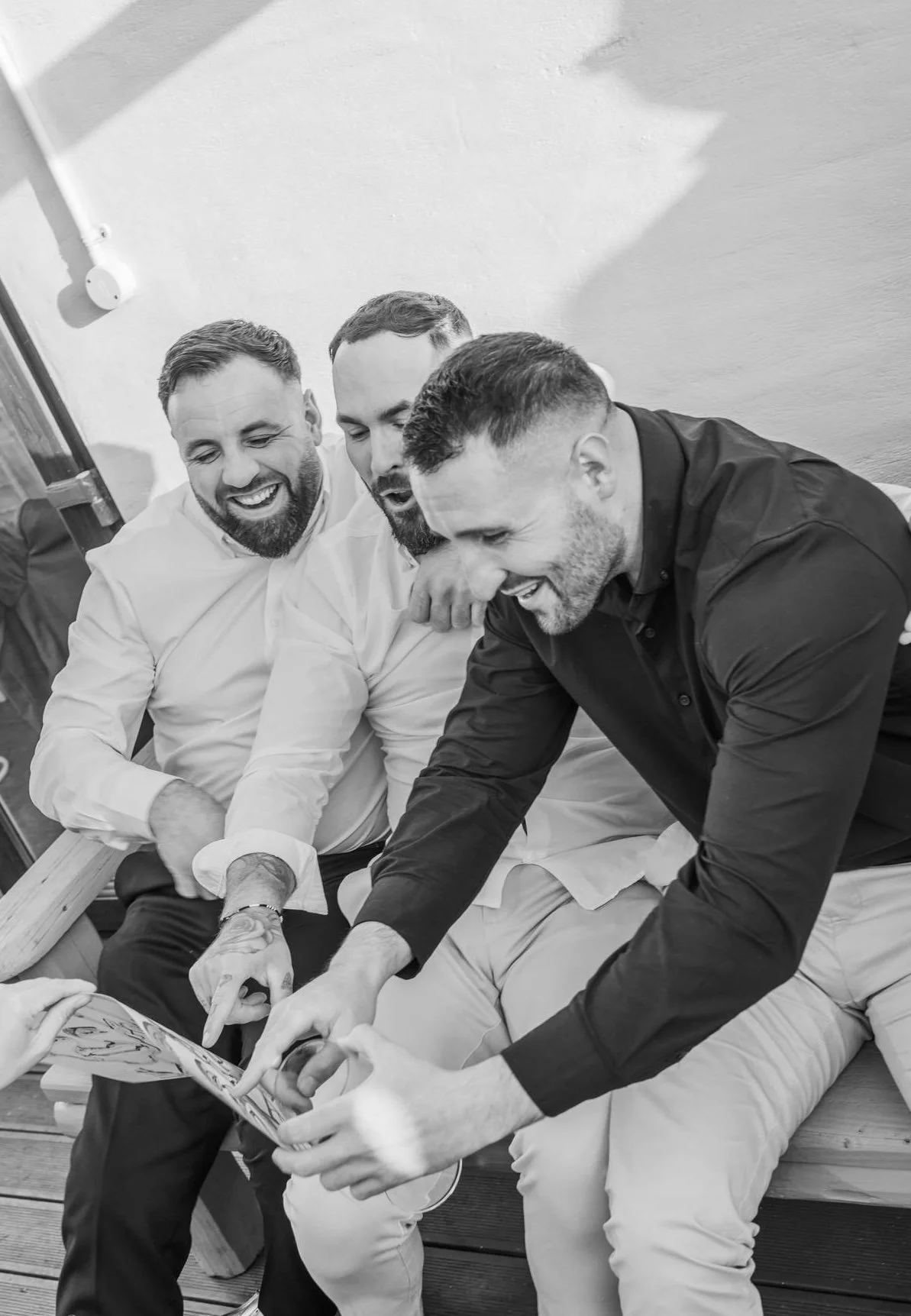 Four men with beards and short hair sitting together on a bench, smiling and looking at a caricature, in a casual setting.