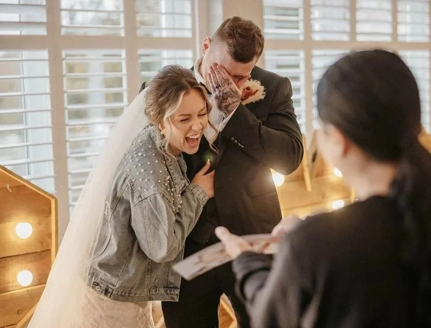 A happy bride and groom at their wedding ceremony, laughing and covering their faces in joy while a caricaturist reveals their portrait.