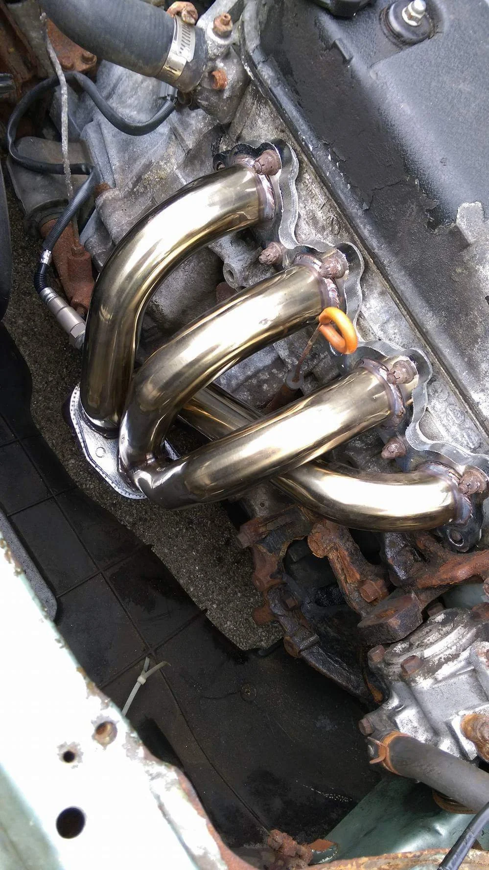 Close-up view of a car engine with new shiny stainless steel exhaust headers installed.