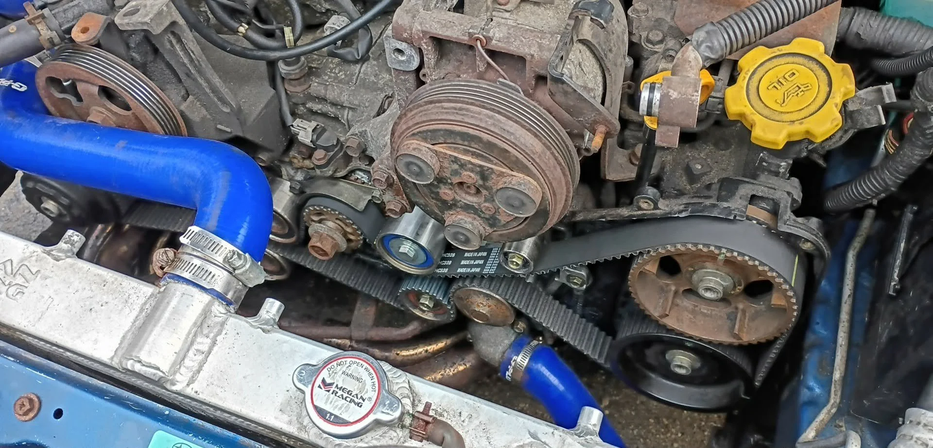 Car engine with visible timing belt, pulleys, and a new blue coolant hose.