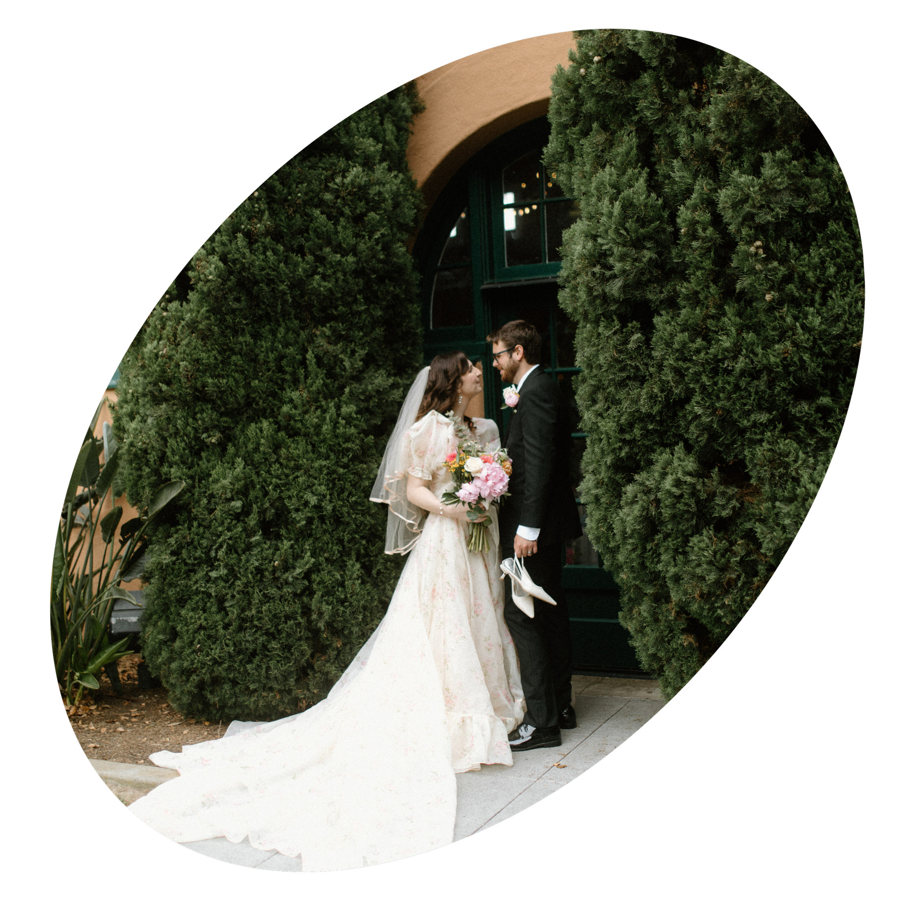 A bride and groom standing close together outdoors, framed by rich green trees, during their wedding celebration.