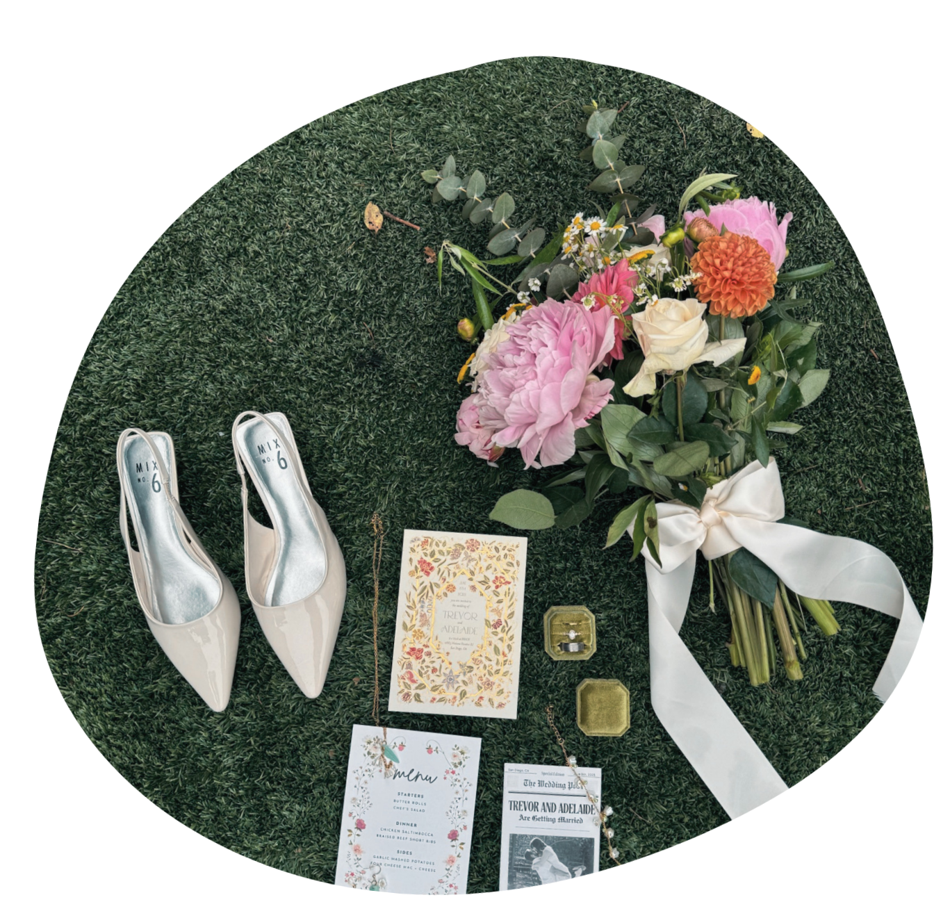 A pair of white high heels, a bouquet of pink, white, and orange flowers with green leaves tied with a white ribbon, wedding invitations, a menu card, vintage jewelry, and a small jewelry box on a grassy surface.