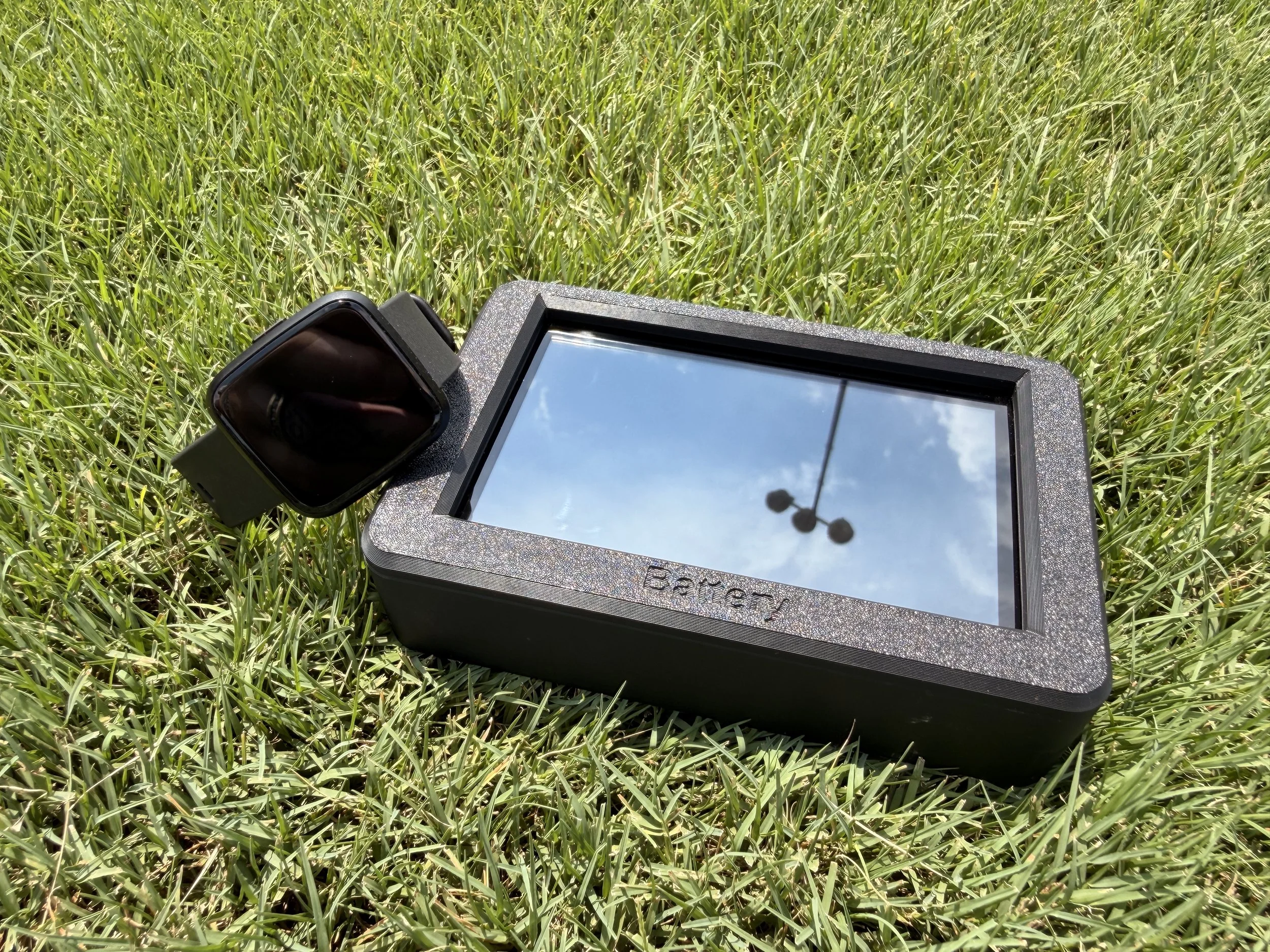 A handheld scanner or measurement device placed on green grass, reflecting the helicopter and sky above.