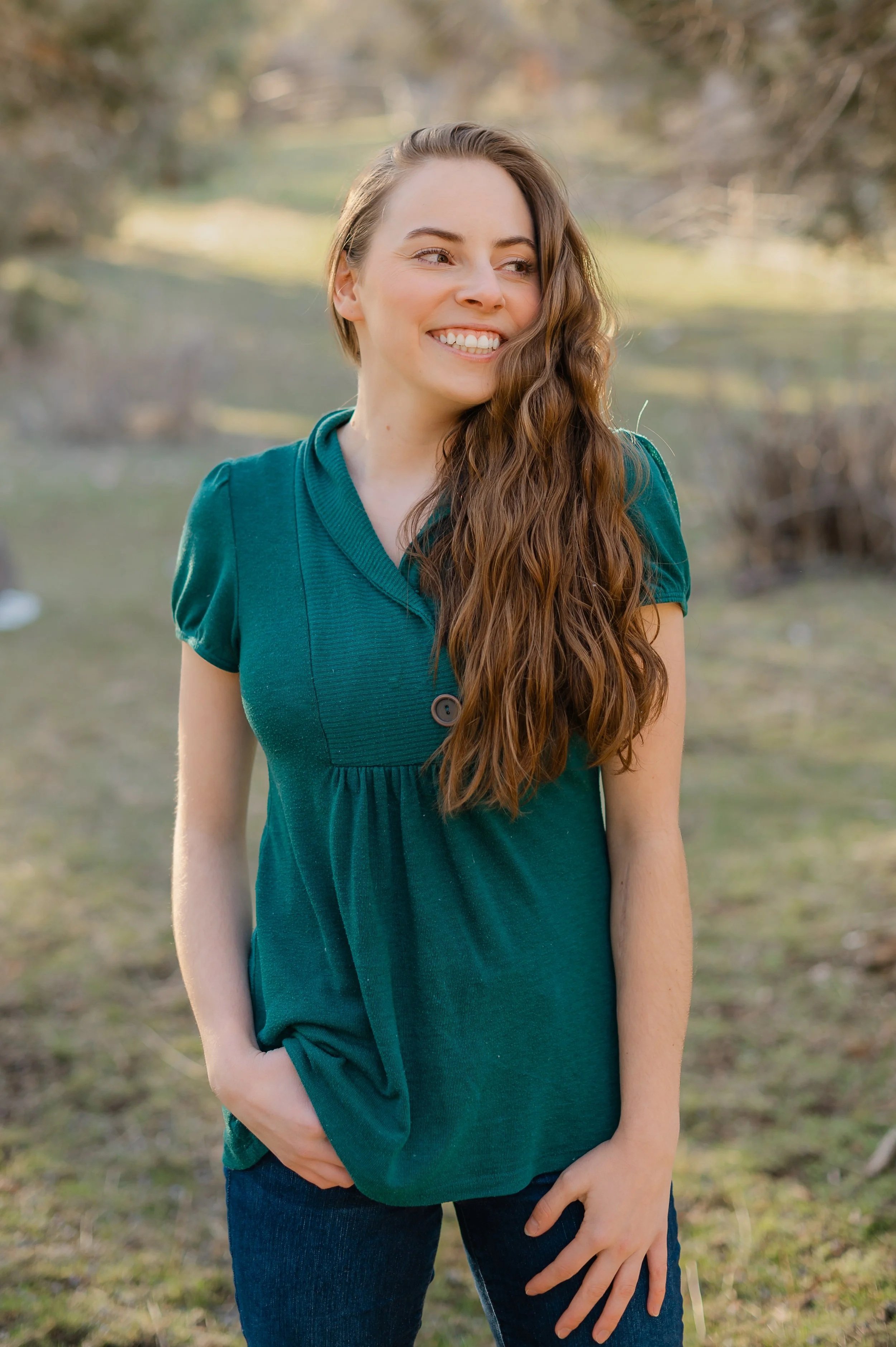 Picture of Trinity standing in a blue shirt with her hair over her shoulder smiling while looking off to the side.