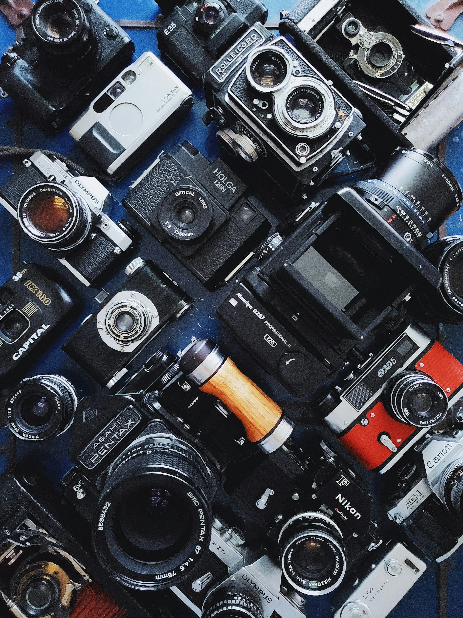 A collection of vintage and modern cameras of various brands and models, including Sony, Olympus, Nikon, and others, arranged closely together on a surface.