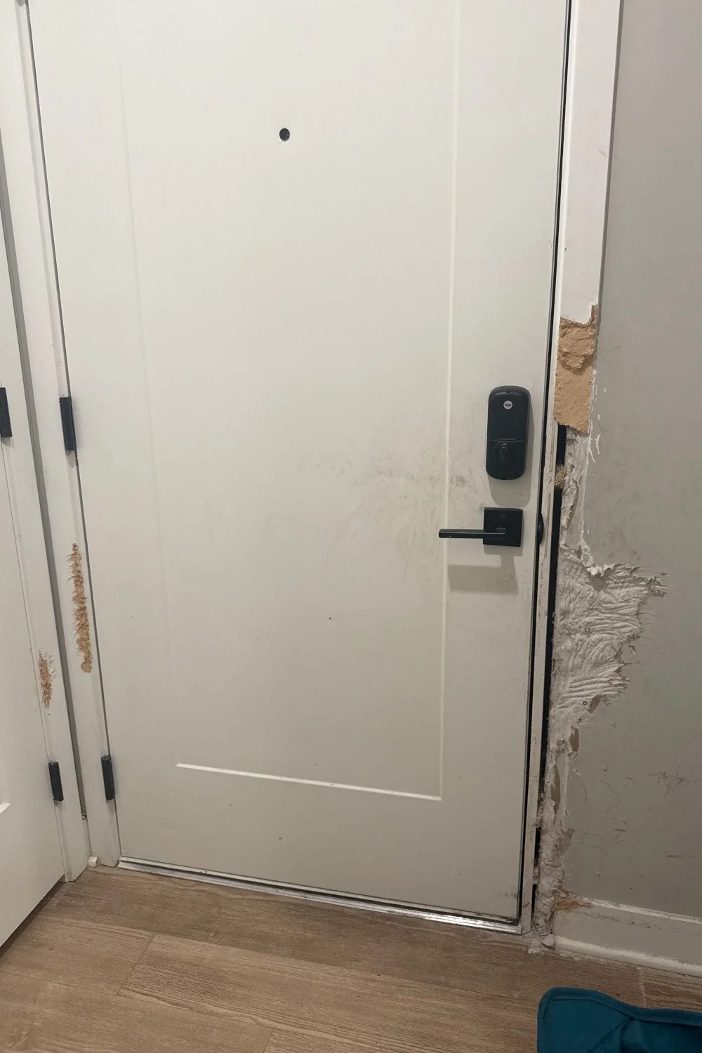 Interior door with electronic lock and damage around the door frame, showing exposed wall and insulation.