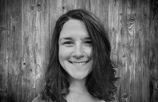 Black and white photo of a young woman smiling in front of a wooden background.