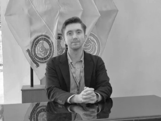 Man sitting at a desk with flags behind him