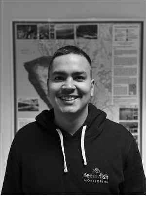 Smiling young man in a hoodie standing in front of a poster.