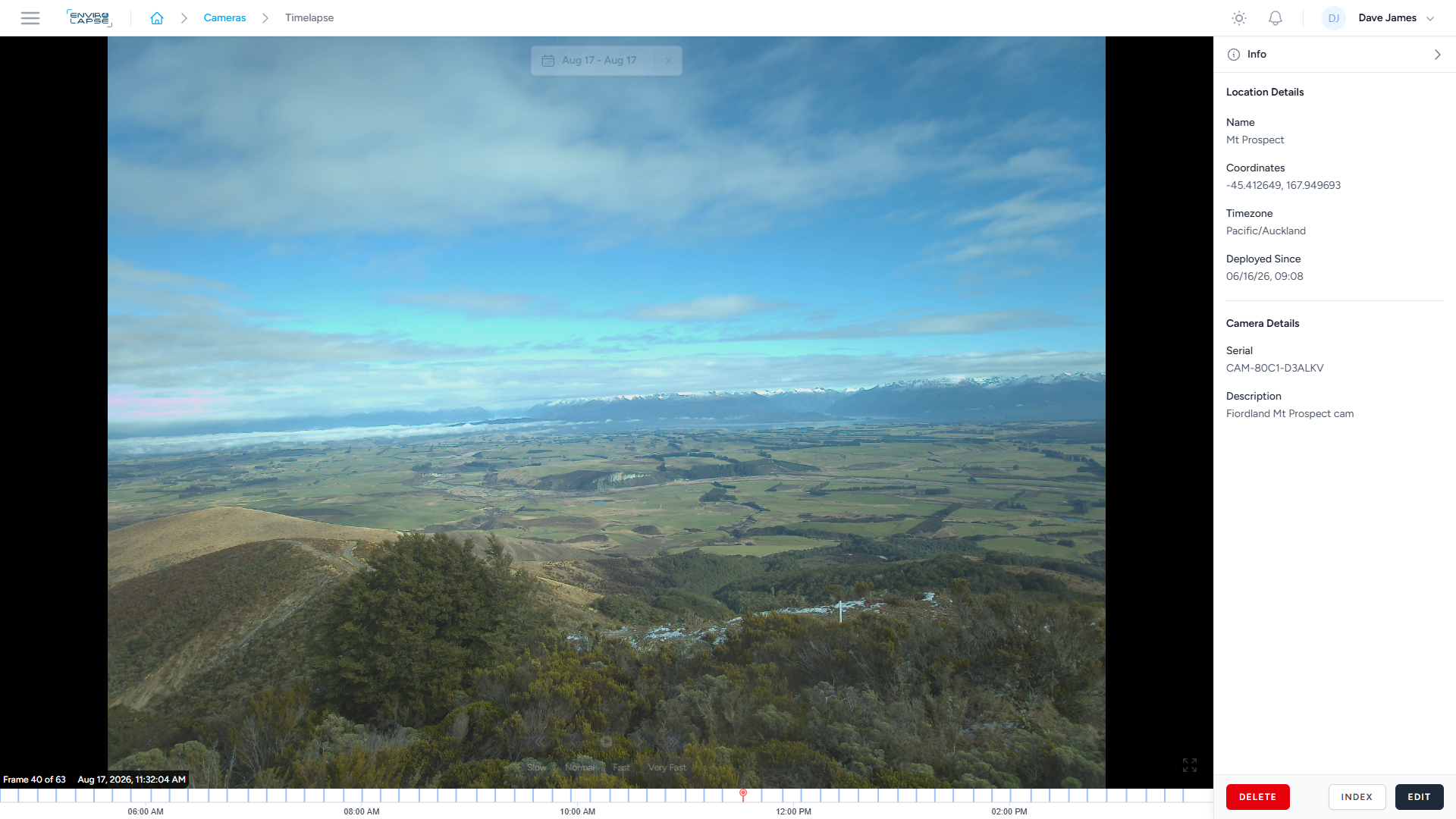 View of a wide valley with green fields, mountains with snow in the distance, and a partly cloudy sky above.
