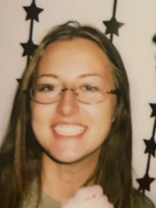 A woman with glasses smiling in front of a wall decorated with black star cutouts.