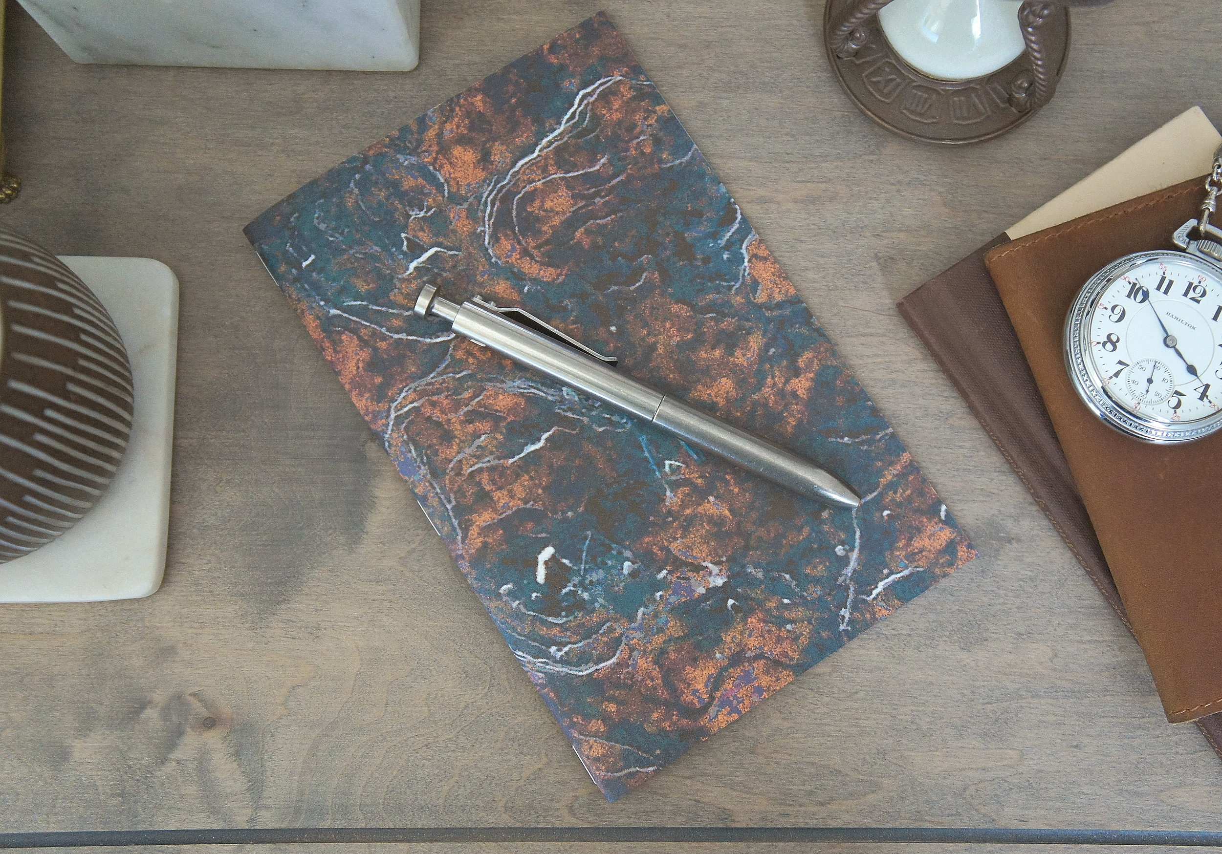 The depiction of mossy stone adorns the outside of a 5 inch by 7 inch softcover journal, handmade in New London, New Hampshire by the Munk Mint